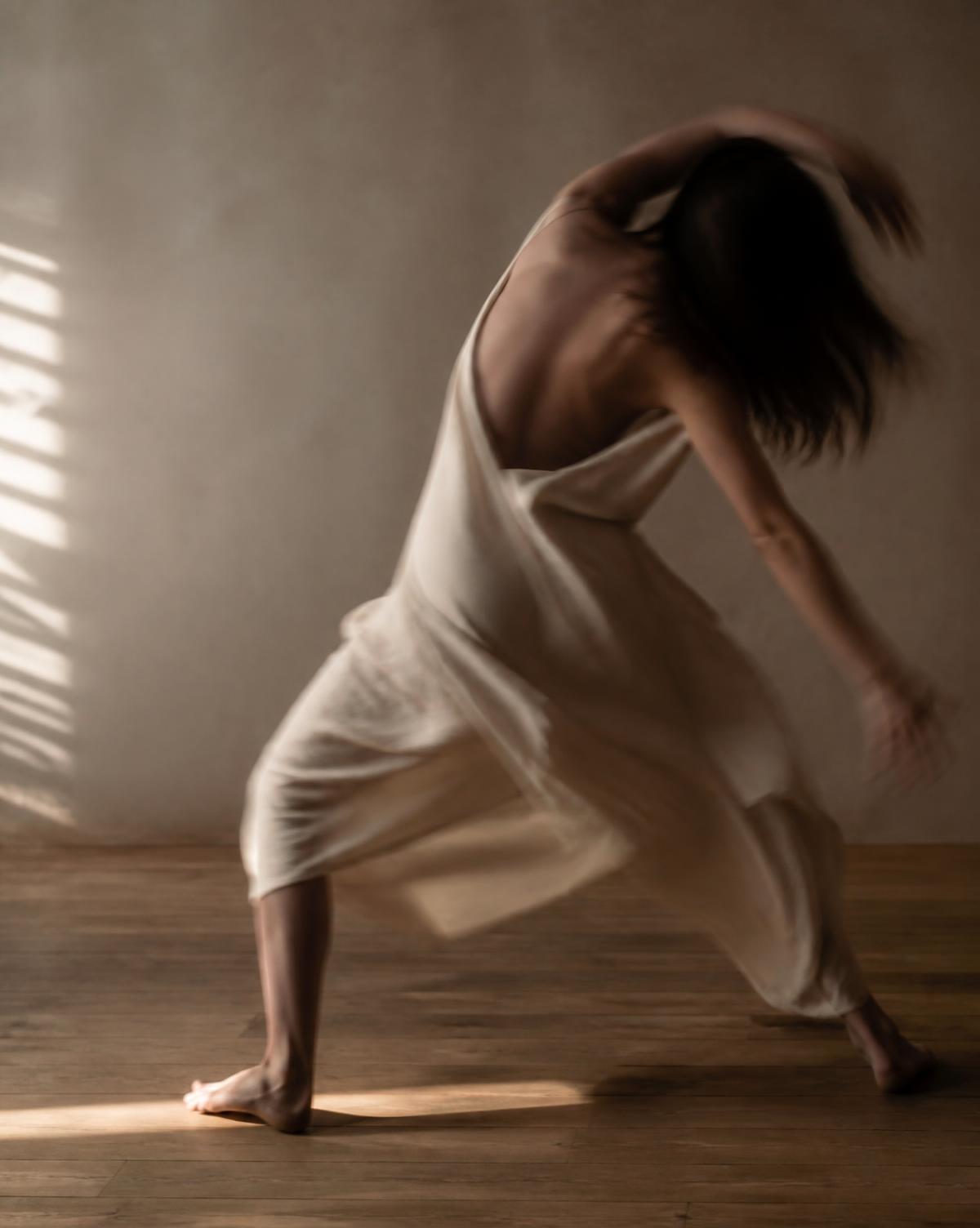 Mujer en movimiento de danza sobre suelo de madera con luz natural